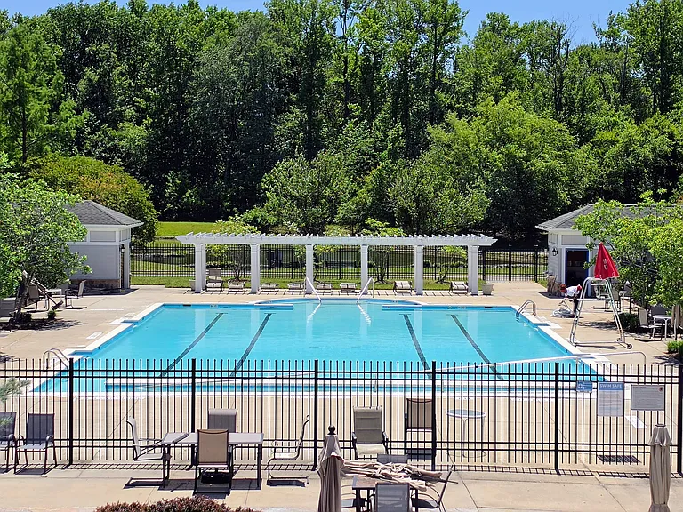 Crystal-clear, fenced-in outdoor swimming pool featuring dedicated lap lanes, lounge chairs, and a scenic tree-lined backdrop.