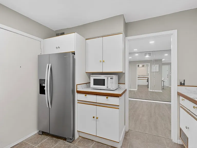 A contemporary kitchen showcasing white cabinets, a refrigerator and a microwave, designed for functionality and aesthetic appeal.