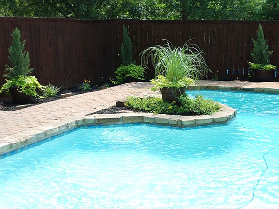 Fenced-in backyard has pavestone around pool & landscaping