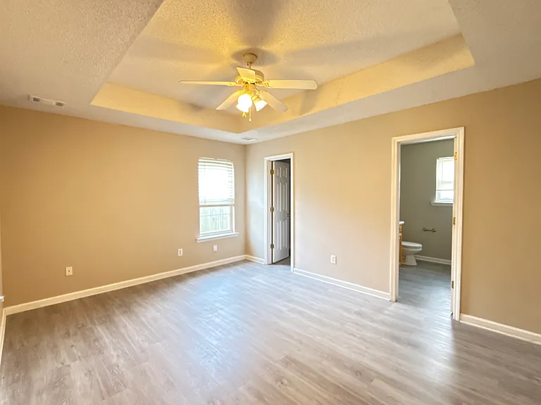 Expansive master bedroom featuring a beautiful tray ceiling, brand-new LVP flooring, and fresh neutral paint