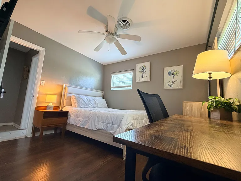 Furnished bedroom nightstand lighting, ceiling fan, and a dedicated desk workspace near the window.