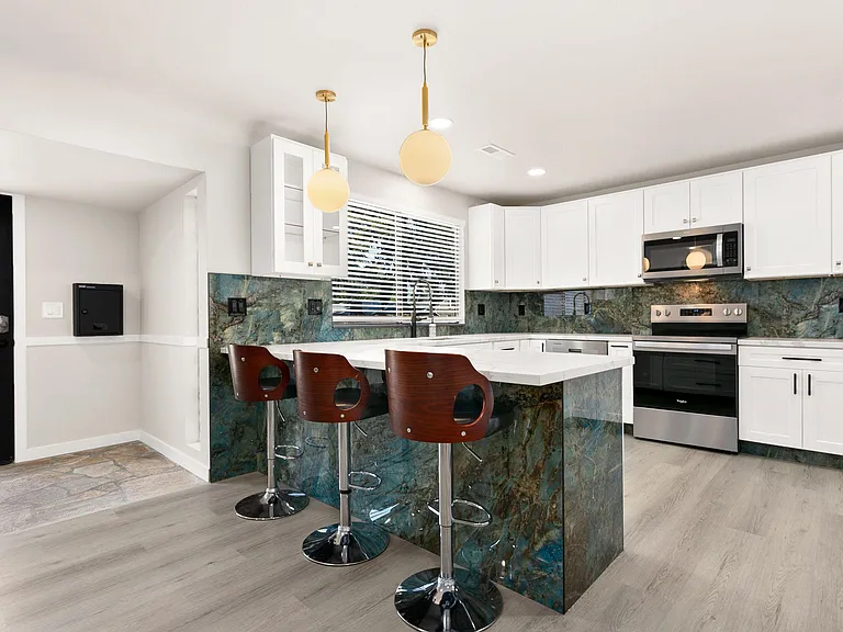 Chef-style kitchen with an oversized breakfast bar, ample white cabinetry, and stainless-steel range and microwave.