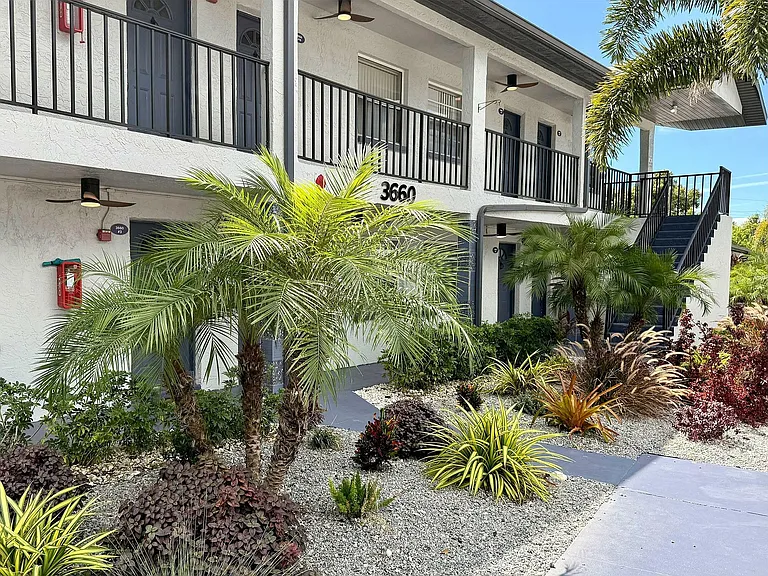 Charming apartment exterior with lush tropical landscaping, featuring vibrant greenery and elegant architectural details.