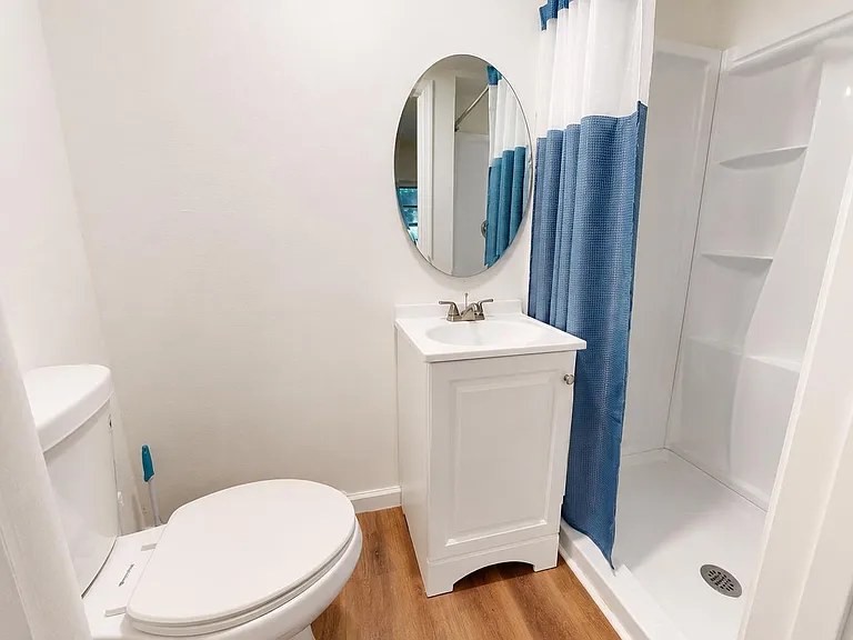 Clean full bath with a single-sink vanity, round mirror, and walk-in shower with built-in shelving.