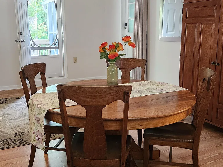Dining area with a round wood table for four, hardwood floors, and convenient access to the exterior door and windows.