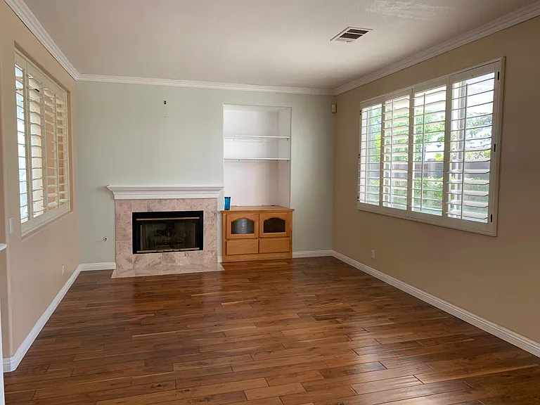 Family room with fireplace, entertainment center, window shutters.