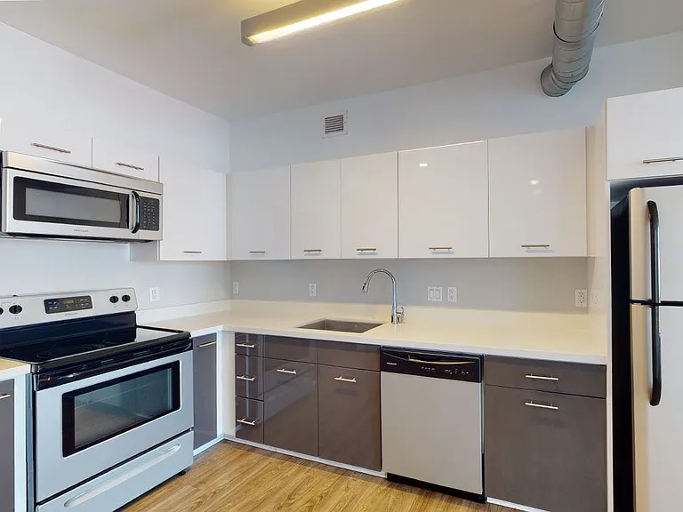 Apartment kitchen with stainless steel appliances, quartz countertops and wood-style flooring.