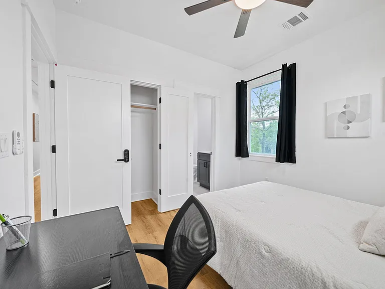 Private bedroom with a bed, desk workspace, ceiling fan, window with curtains, and closet storage; nearby bath access.