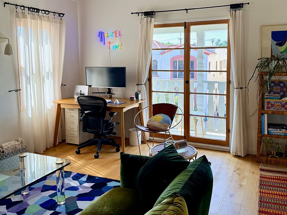 The living room workspace features an oversized monitor, Herman Miller Aeron chair, and double French doors leading to the balcony.