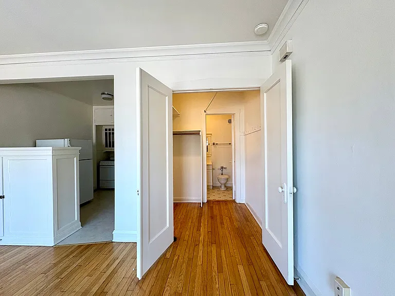 Inviting apartment interior showcasing a bright hallway with wooden flooring, leading to a kitchen and bathroom, featuring elegant white doors. Inviting apartment interior showcasing a bright hallway with wooden flooring, leading to a kitchen and bathroom