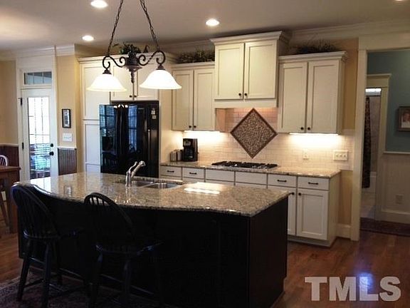 Large island with breakfast bar seating, cascading cabinets with under cabinet lighting, gas cooktop, subway tiles with decorative tile piece.