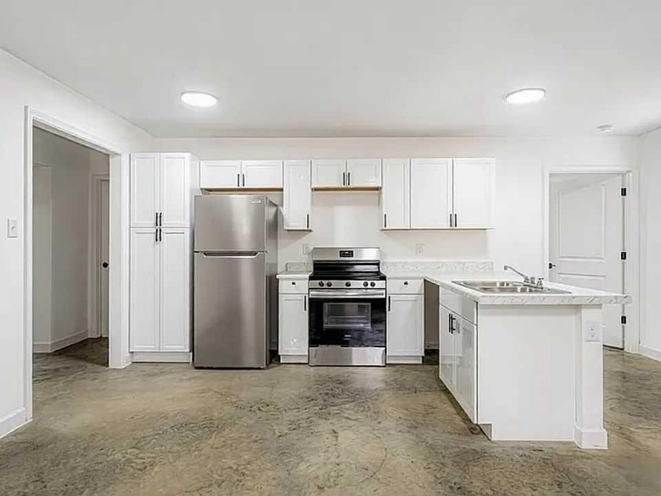 A bright, open-concept kitchen featuring crisp white cabinetry, stainless steel appliances, and industrial-chic polished concrete floors.