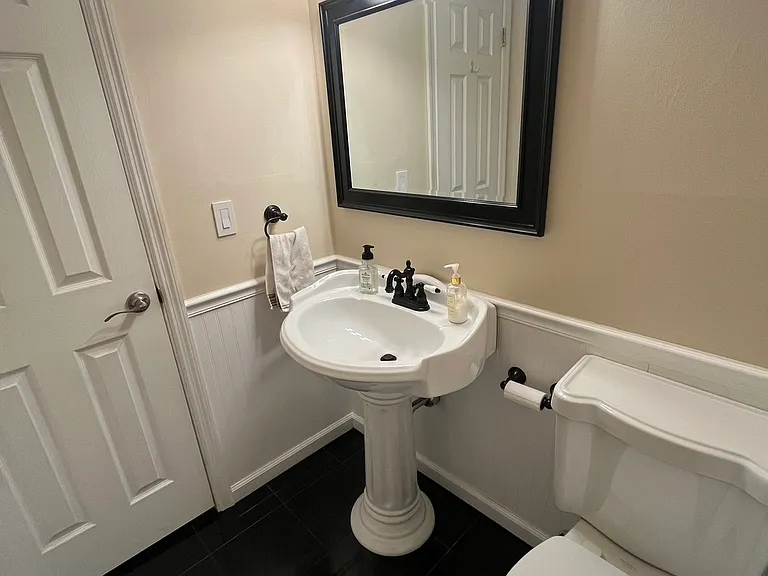 Striking downstairs half bath for guests. Black marble floor and matching pedastal sink and porcelain throne.