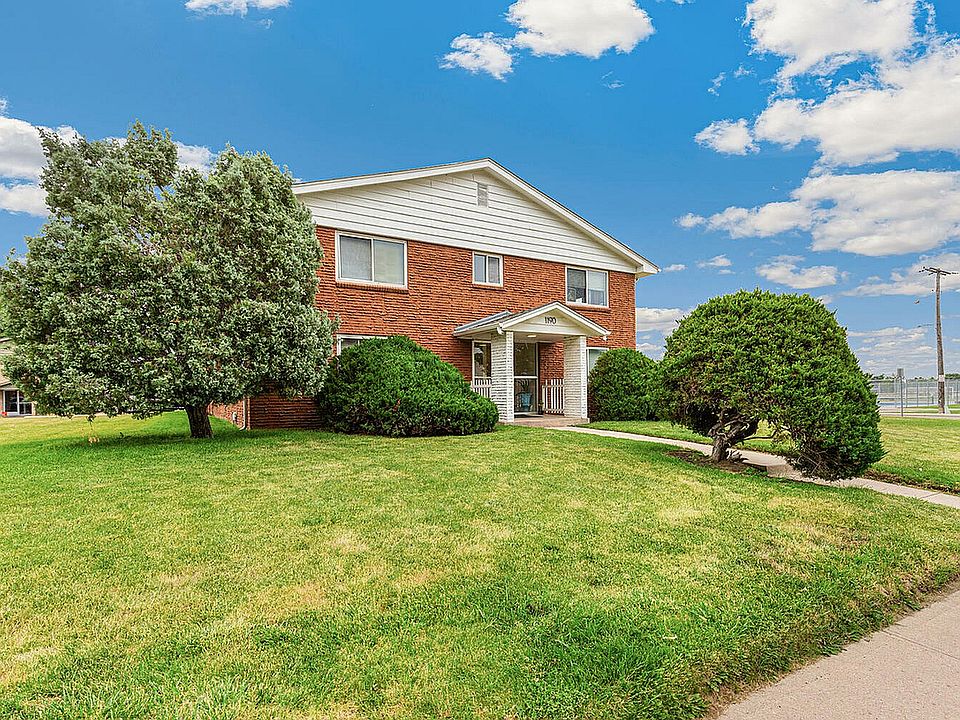 Charming red-brick duplex surrounded by lush green lawn and vibrant trees under a bright blue sky.