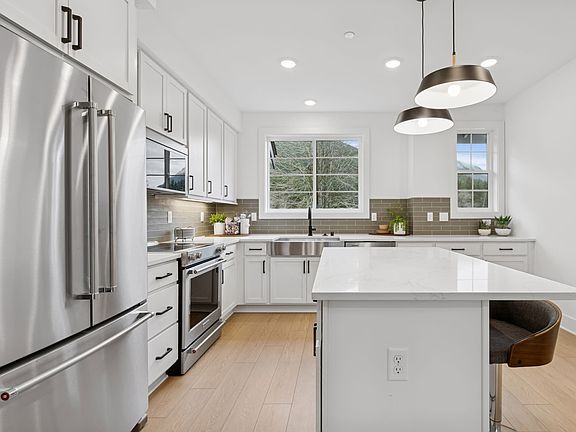A modern, well-lit kitchen with stainless steel appliances, white cabinets, and a central island wit