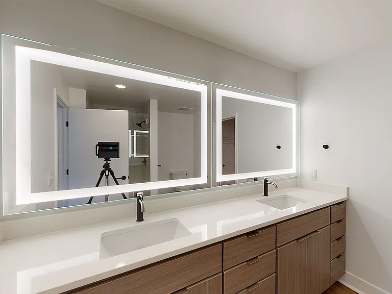 Apartment bathroom with wood-style flooring, double sinks and LED vanity mirror.