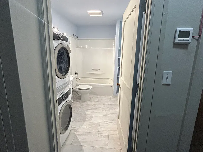 Bathroom: in-unit washer and dryer, shower and tub, toilet, vanity and mirror, and storage spaces
Also pictured: apartment thermostat