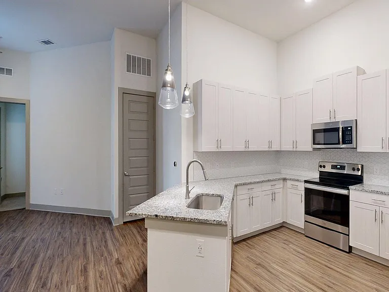 Apartment Kitchen with Stainless Steel Appliances, Dining and Living Room with Wood Style Flooring.