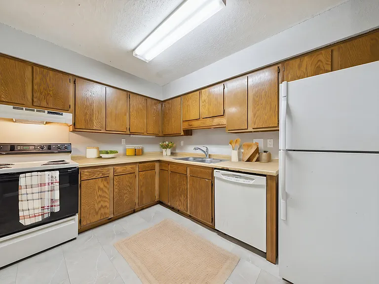 Kitchen (unit is not furnished) with stove, dishwasher, refrigerator, and vent fan.