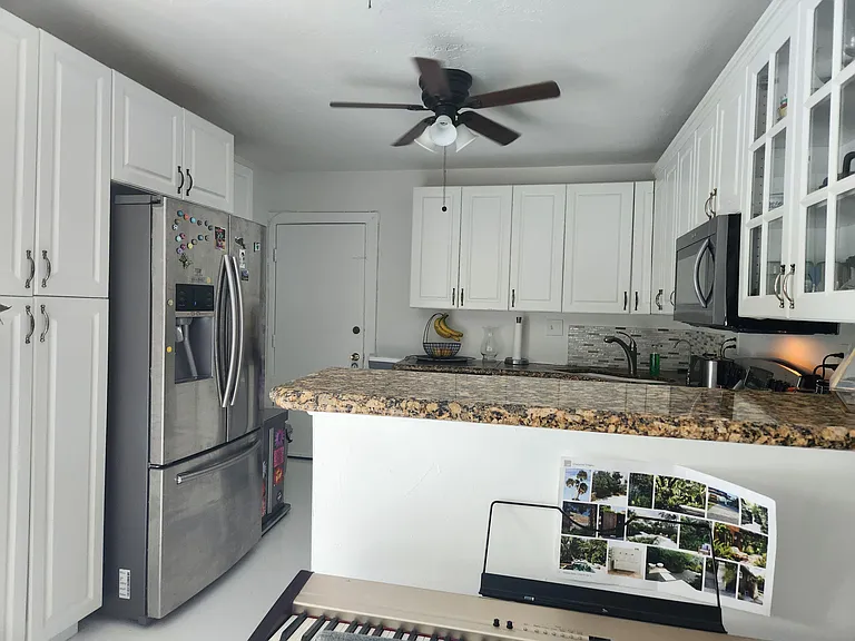 Kitchen with ample white cabinetry, granite-look counters, mosaic backsplash, and stainless steel refrigerator and microwave.