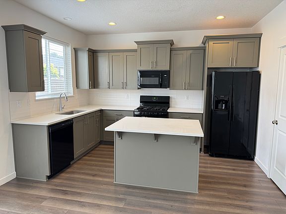 Kitchen with new microwave oven, dishwasher, side-by-side refrigerator, gas range, island and quartz countertop.