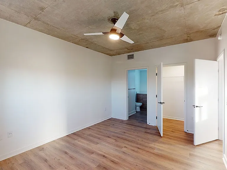Spacious apartment bedroom with large closet, attached bathroom and wood-style flooring.