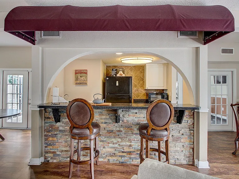 Cozy and elegant kitchen area with stone-faced breakfast bar, leather bar stools, and warm lighting, seamlessly connecting to the dining space.