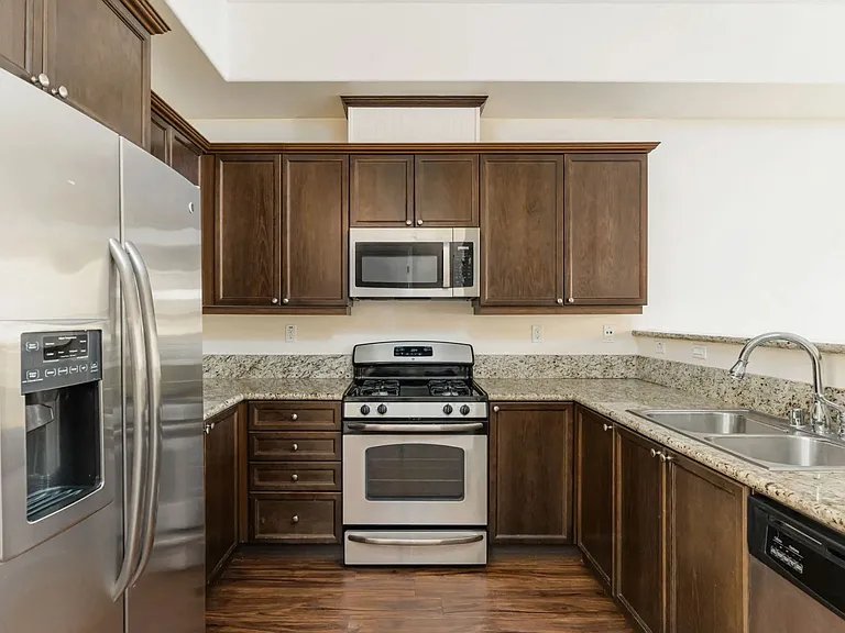 Kitchen with stainless steel appliances, granite slab counter tops, and spacious dark wood cabinets at The Nines Townhomes in Escondido, California.
