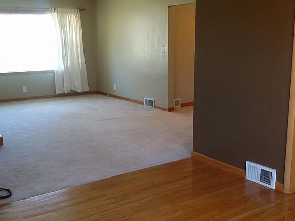 View of carpeted living room from hardwood floor dining room. Painted walls are all shades of biege.