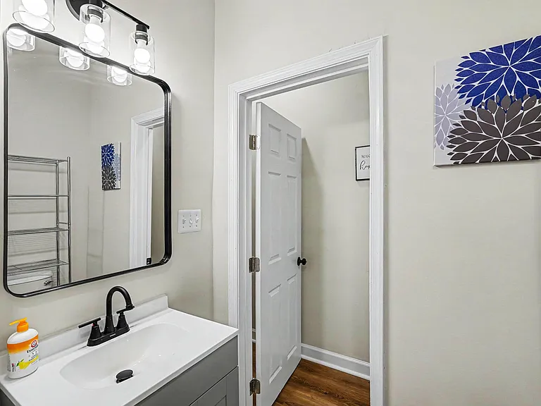 Updated vanity area with a framed mirror, modern light fixture, and convenient storage shelving for toiletries and linens.