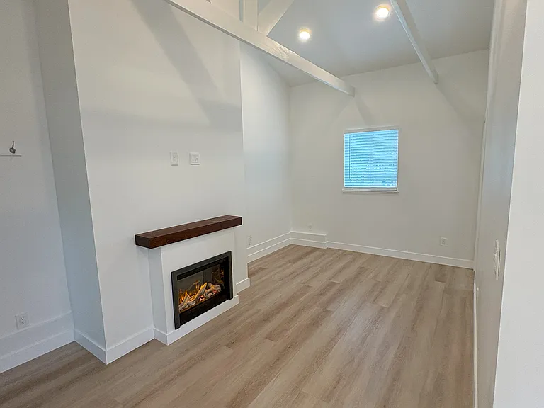 Living room viewed from kitchen has an electric fireplace/heater. South-facing window views the driveway.