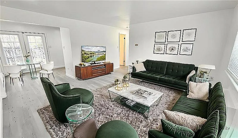 Elegant living room with plush green velvet sofas, a chic coffee table, and wall art; adjacent dining area with large windows letting in abundant natural light. - OAK NORTH APTS
