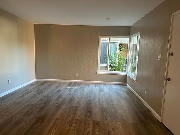 Living room view with windows looking out towards entry courtyard. Front door is visible on the right wall.