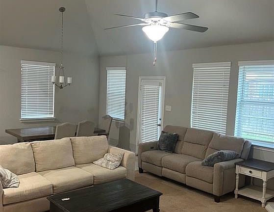 Living area featuring vaulted ceiling, a chandelier, light carpet, and ceiling fan