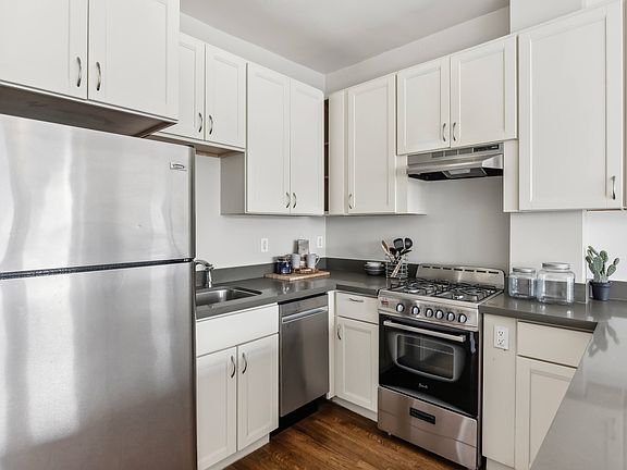 Kitchen with multiple cabinets, refrigerator, stove, range hood, and sink