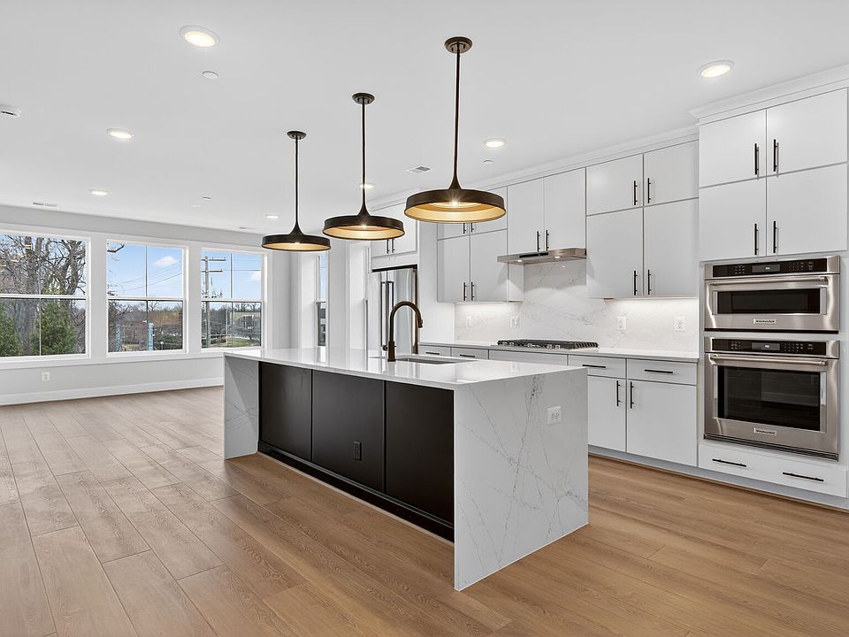 A modern, open-concept kitchen with white cabinets, a large island, and pendant lighting fixtures, s