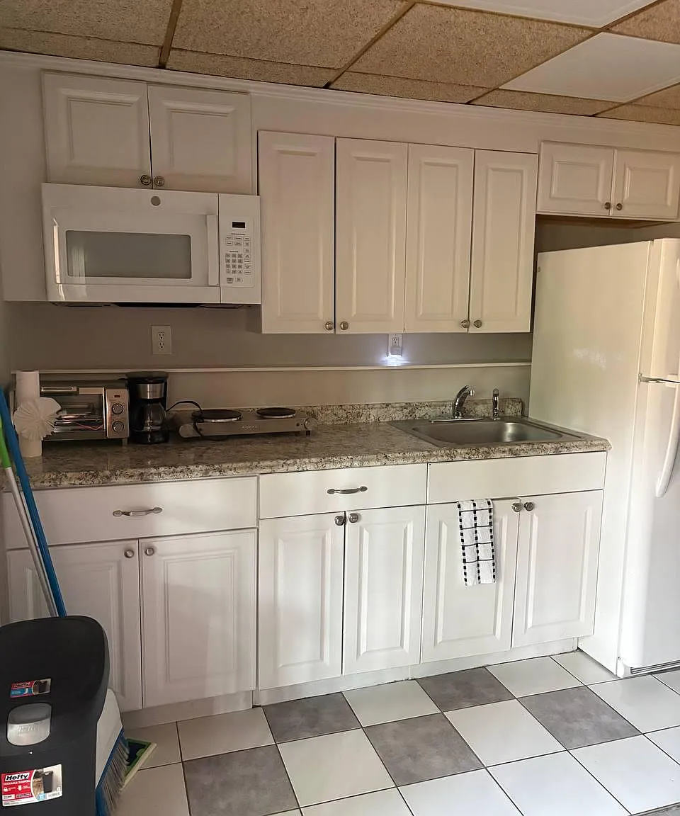 Efficient kitchen with ample white cabinetry, laminate counters, sink, microwave, and full-size refrigerator for easy meals.