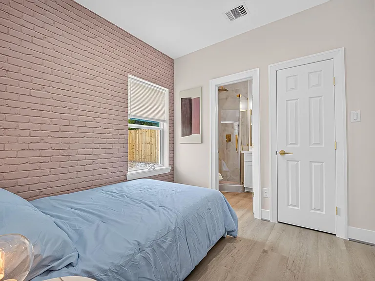 Bedroom with a painted brick accent wall, large window, and easy access to an en-suite bath and closet.
