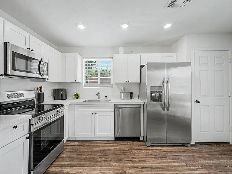 Well-appointed kitchen with white cabinetry, generous counters, and stainless steel appliances plus a window-side sink.