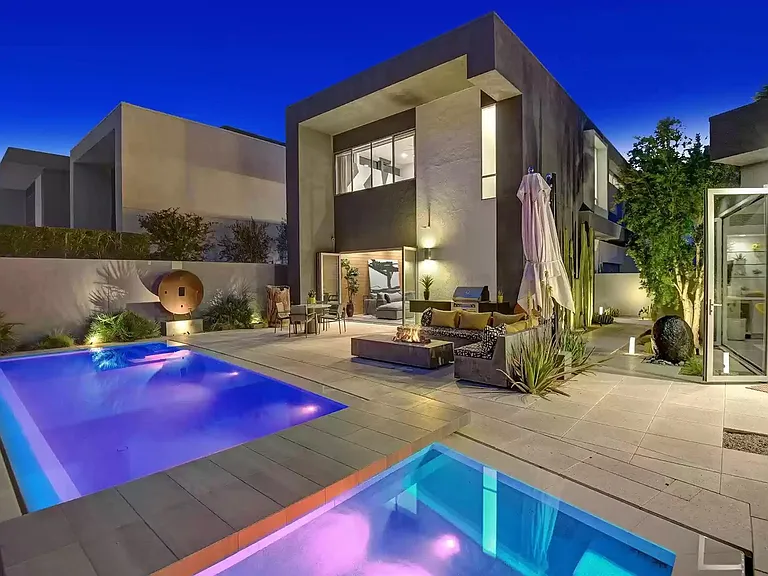 Backyard at night with a pool, spa and casita. Lit fire pit and built in seating.