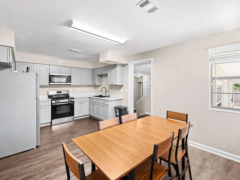 Eat-in kitchen with ample cabinetry, stainless appliances, and a dining table set beside a large window.