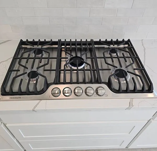 Detailed view of stainless steel gas cooktop, pot filler, and light countertops