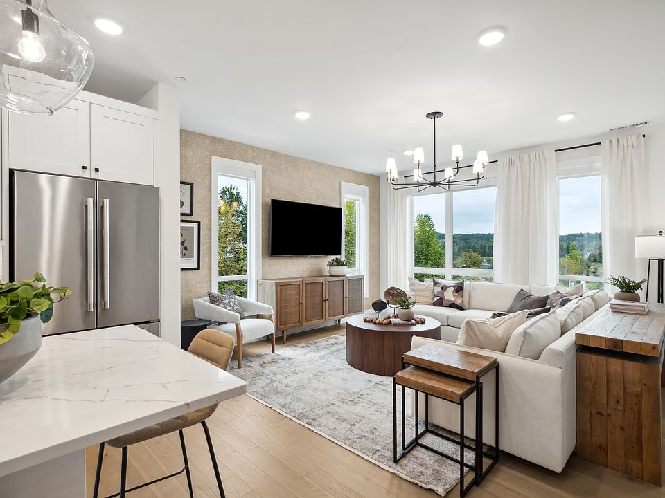 A modern and spacious living room with a kitchen area, featuring a large window overlooking a scenic