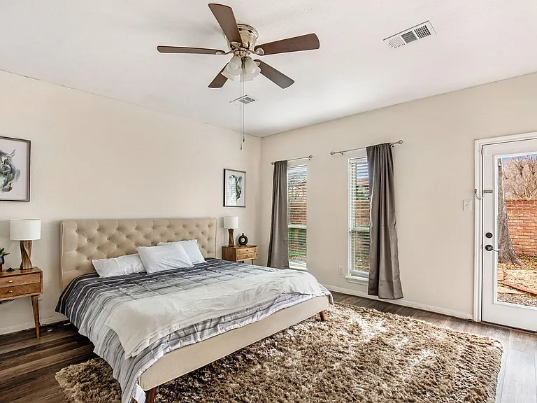 Spacious bedroom with a king bed, ceiling fan, large windows, and a private exterior door for easy access and convenience.