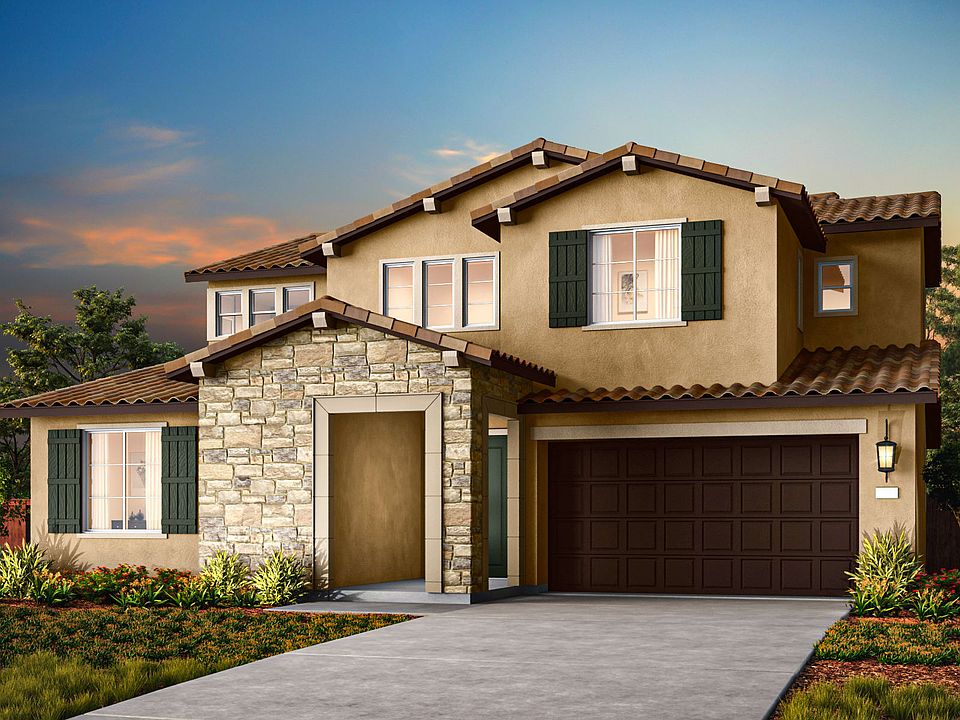 A two-story Mediterranean-style house with a stone exterior, a tiled roof, and a garage door stands