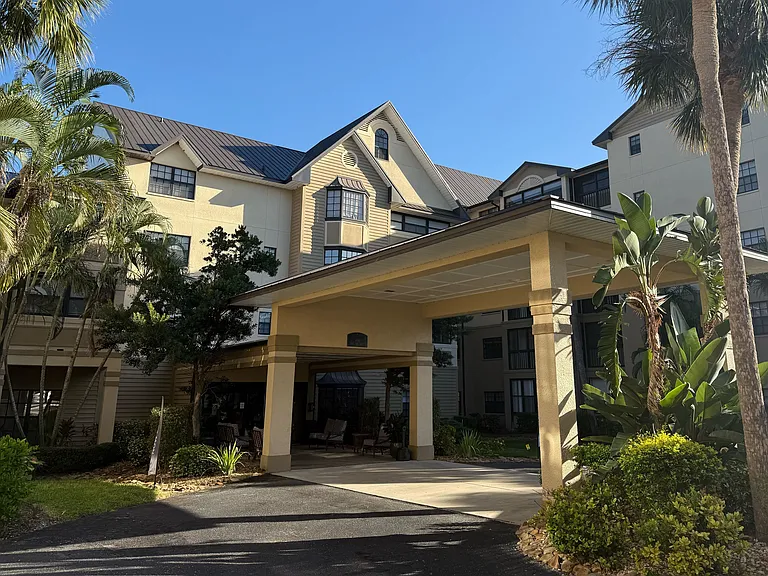 Charming apartment building with elegant architecture, surrounded by lush tropical landscaping and a welcoming driveway.