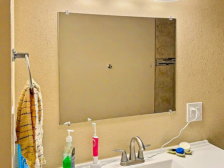 Bathroom vanity area featuring a wide mirror, overhead three-light fixture, and a clean white sink with chrome faucet.