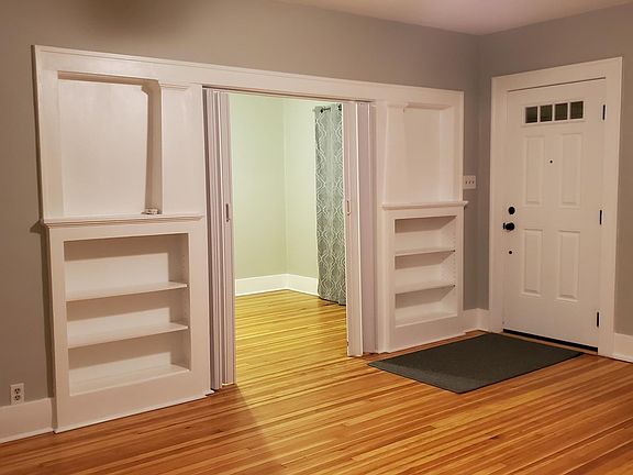Living room with custom built in shelving and original hardwood floors leads to master bedroom. Custom front door.