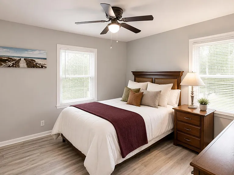 Spacious bedroom with two large windows, ceiling fan, and a nightstand for convenient bedside storage.