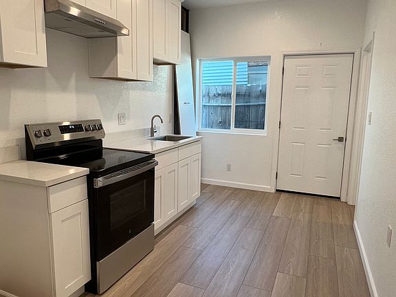Interior view of Garage Junior ADU- brand new kitchen with white quartz countertop, white cabinets, sink, stove, hood, recess lighting and new hardwood floors.